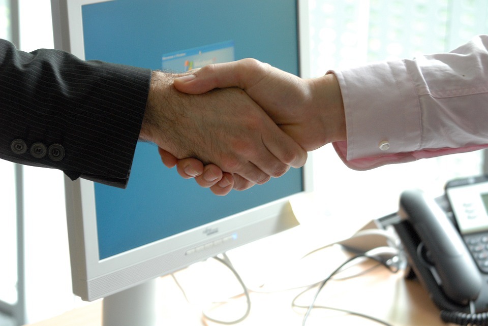 Dos manos se estrechan ante la pantalla de un ordenador tras la firma de un contrato de trabajo