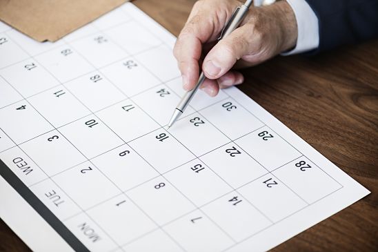 Un hombre consulta en un calendario la fecha de renovación de su certificado digital y tiene la intención de realizar anotaciones en el mismo con su bolígrafo